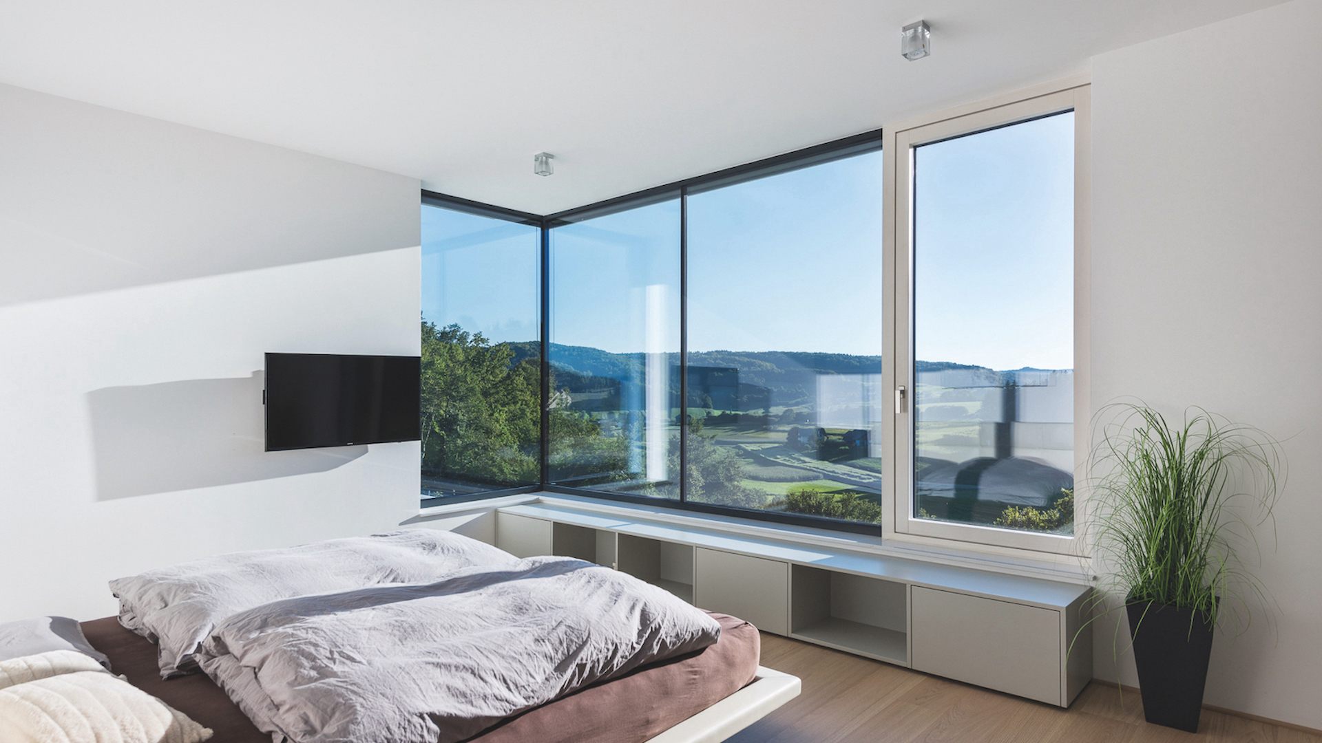 Modernes Schlafzimmer mit bodentiefen Aluminium-Fenstern und großzügiger Panorama-Verglasung – hochwertige Fensterlösungen in Esslingen für lichtdurchflutetes Wohnen und effektiven Sonnenschutz.